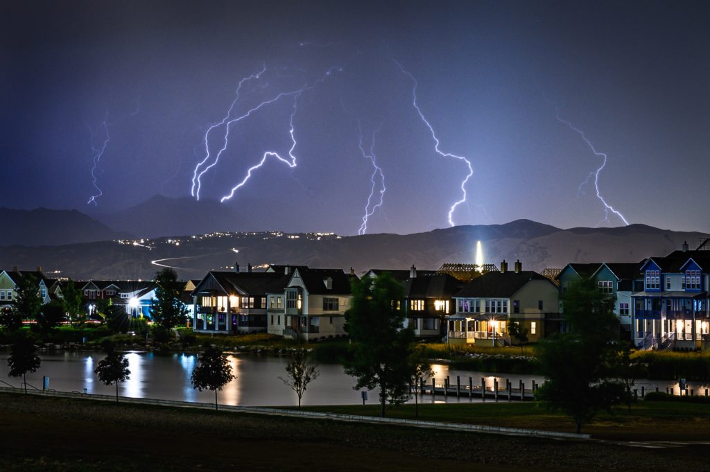 multiple lightning bolts strike the hilltop behind a city