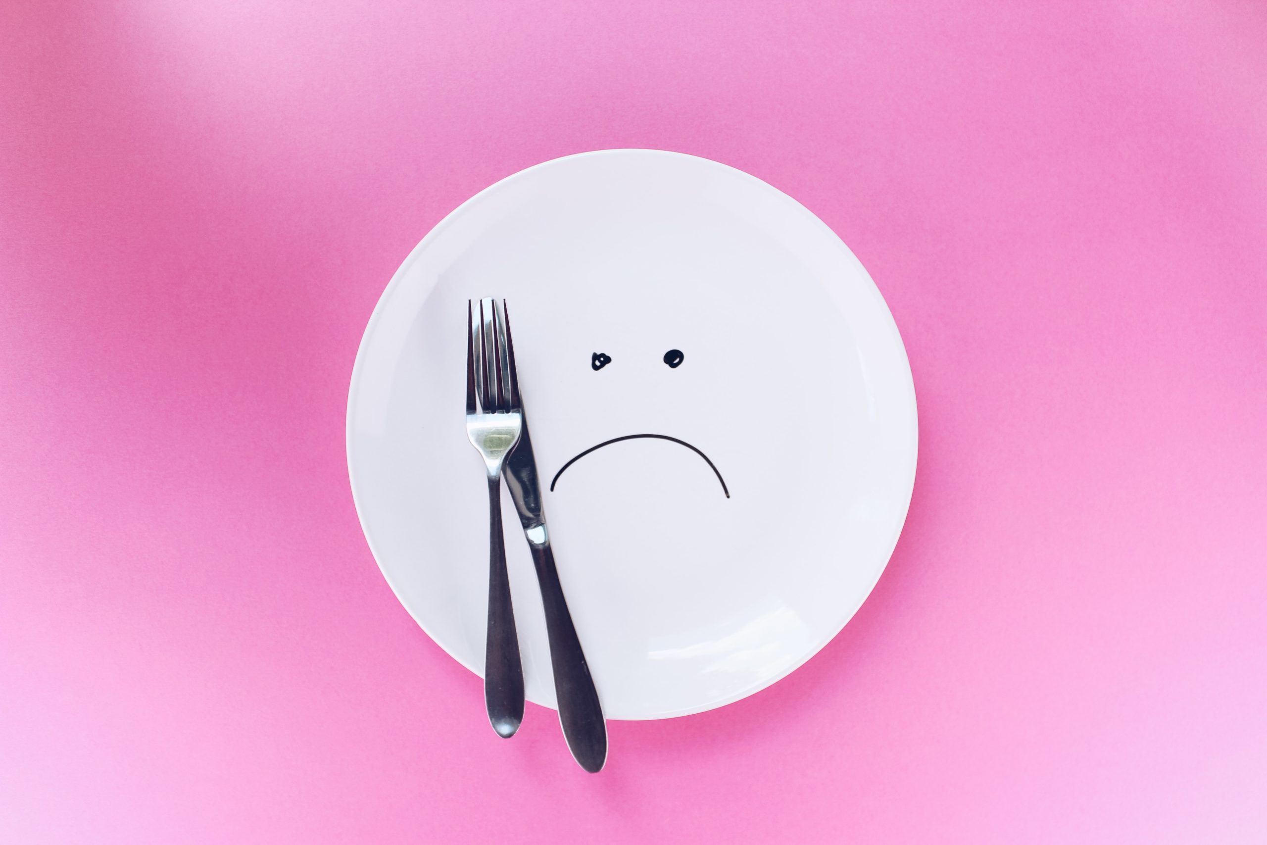 plate with a sad face drawn on it over a bright pink background